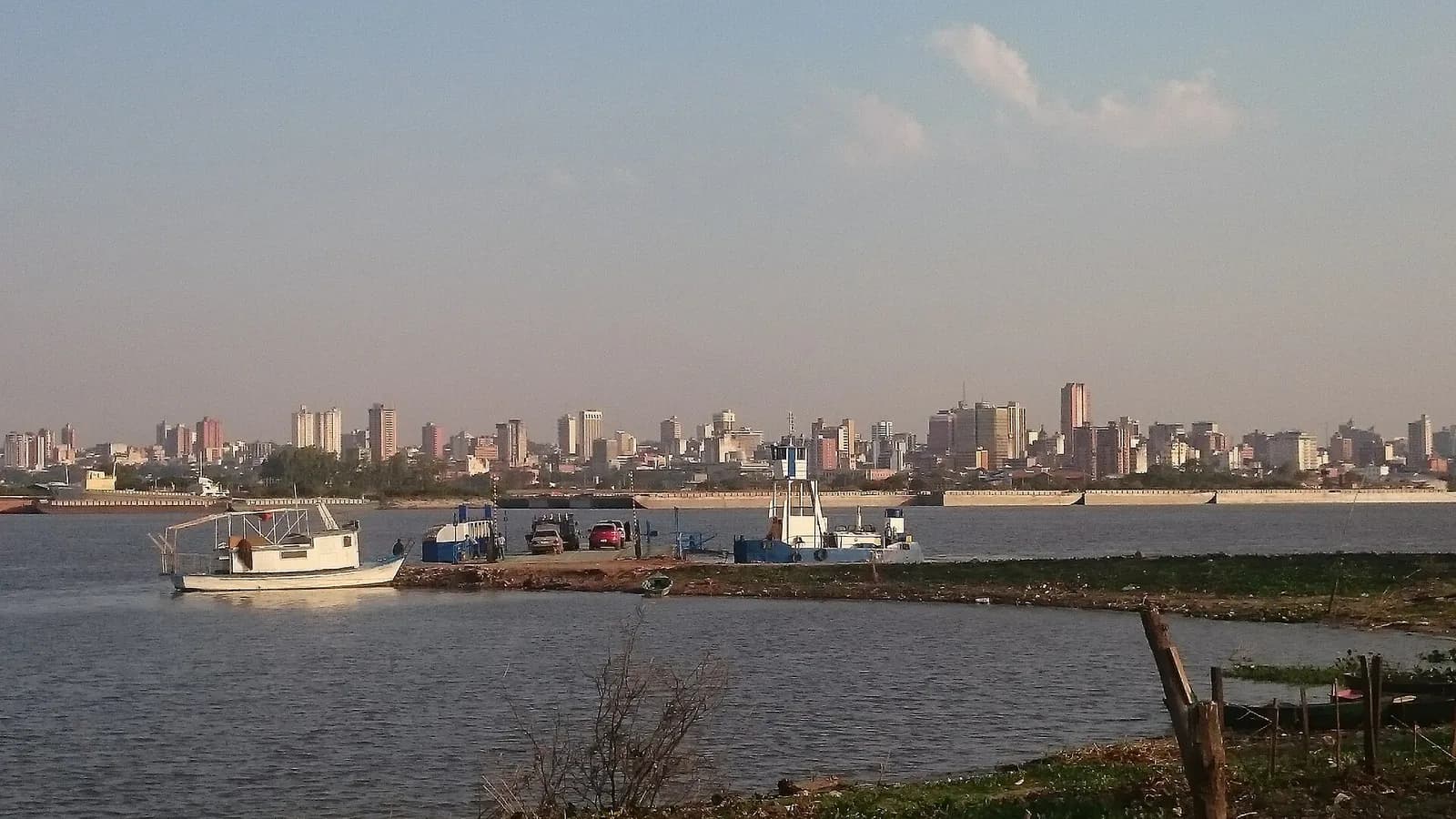 Skyline d'Asunción vue depuis l'autre rive du río Paraguay, avec un bac et une barge au premier plan