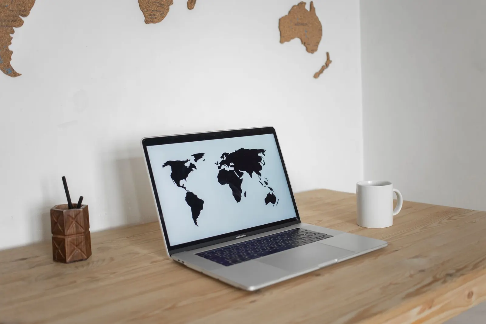 Ordinateur portable affichant un planisphère sur un bureau en bois, devant une carte du monde murale