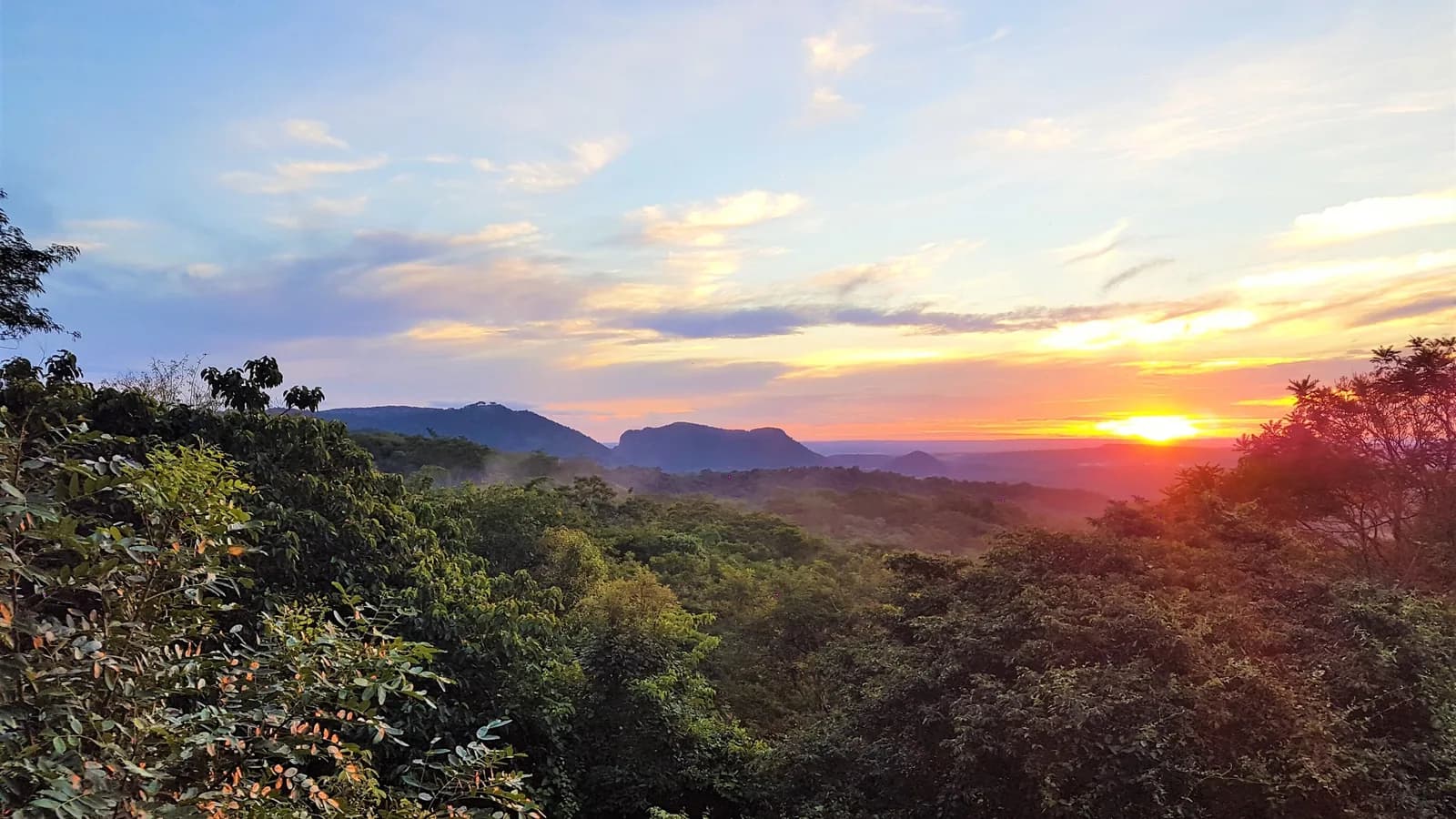 Coucher de soleil depuis le mirador de la réserve Mbatoví, au Paraguay : collines boisées et ciel orangé