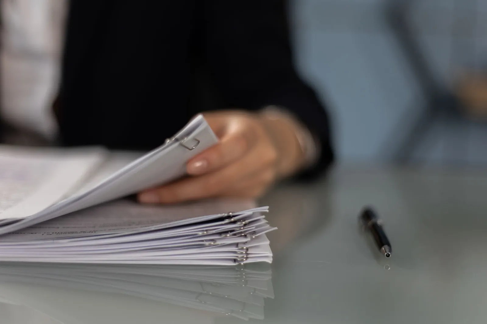 Main feuilletant une pile de dossiers agrafés sur un bureau, à côté d'un stylo