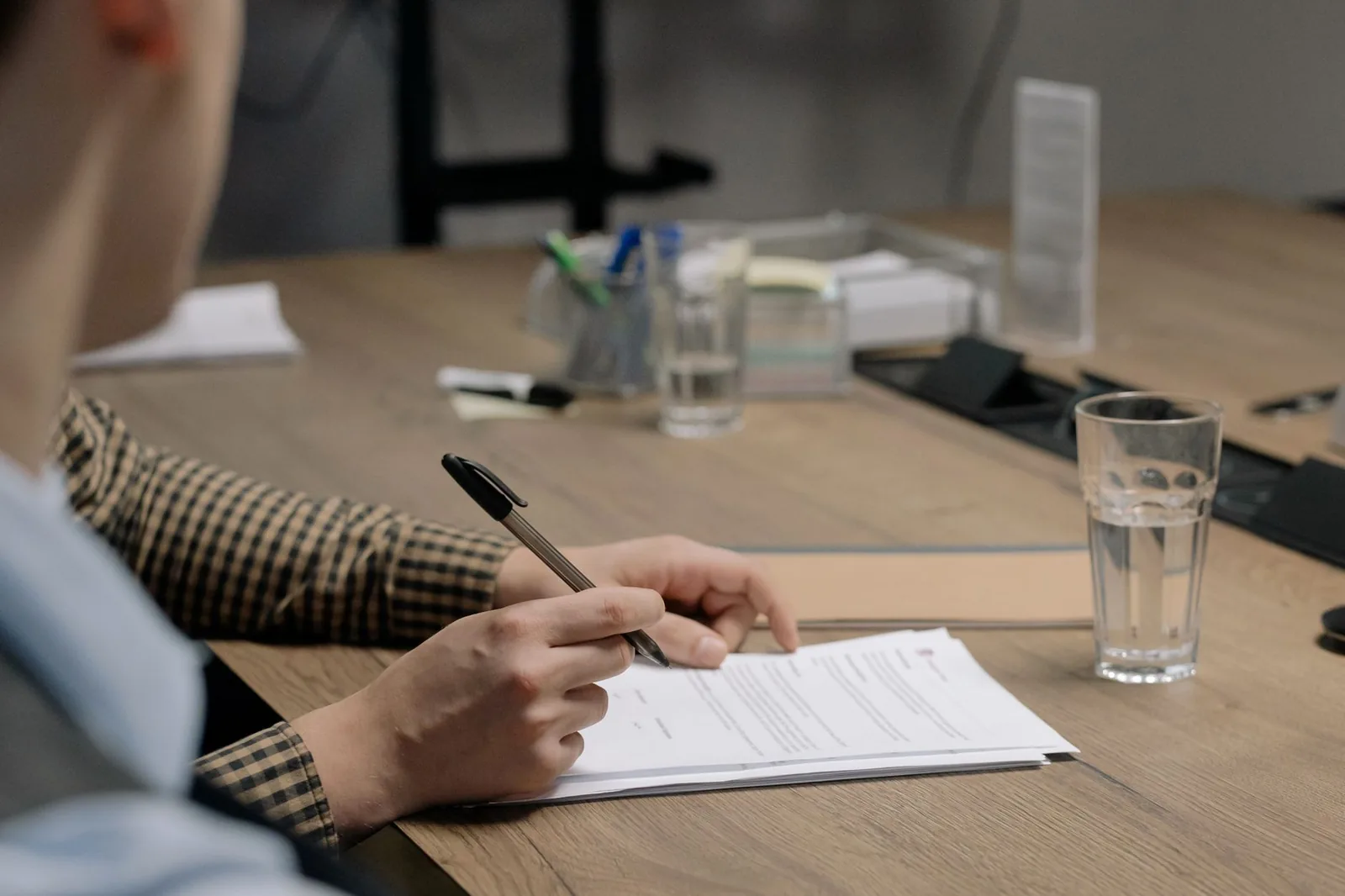 Personne signant un document avec un stylo sur un bureau, un verre d'eau à côté