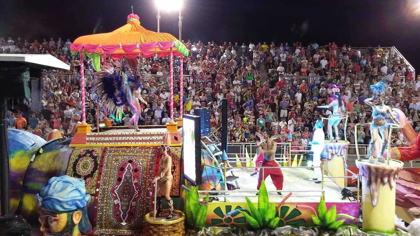 Char et danseurs costumés devant les gradins pleins du sambodrome lors du carnaval d’Encarnación, au Paraguay
