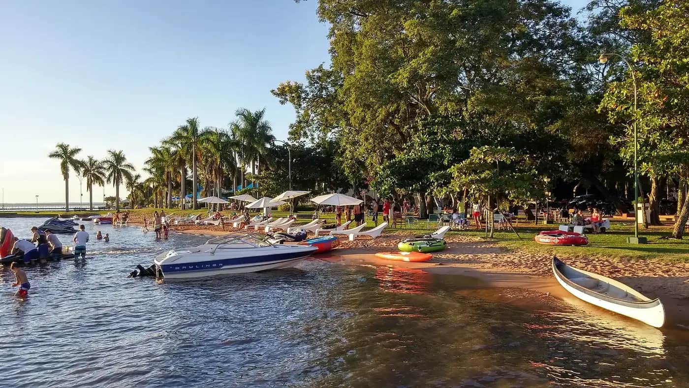 Plage de sable du lac Ypacaraí à San Bernardino, avec palmiers, bateaux à moteur et baigneurs en fin de journée